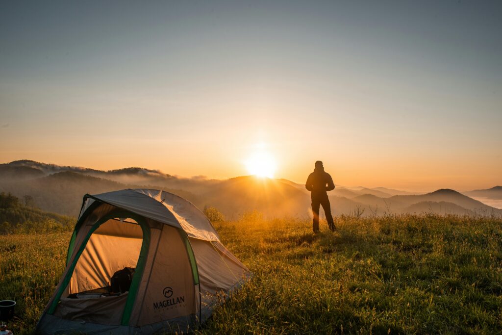 A camper enjoys the sunrise in a mountain setting with a tent. Perfect nature escape. Traveling with no money